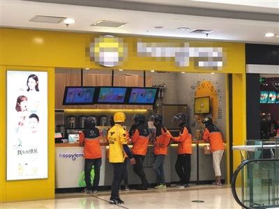 4月12日,一家饮品店门前等待取外卖的滴滴外卖骑手与路过的美团外卖骑手。摄影/新京报记者 陈维城