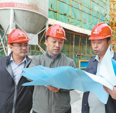 门盛庆(中)在某项目施工现场了解建设进度。资料照片