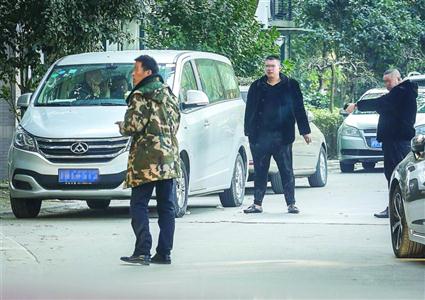 讨债者(着黑衣的两人)以面包车为据点守在109号楼前,小区保安(着迷彩服)经过109号楼。 晨报记者 张佳琪