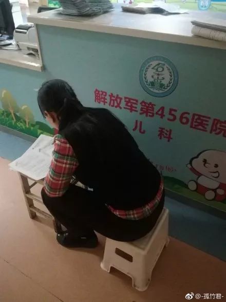 南一女老师陪娃住院,走廊趴板凳上批改试卷到