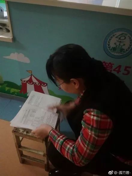 南一女老师陪娃住院,走廊趴板凳上批改试卷到