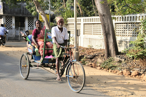 资料图片：2013年1月11日，在印度本地治里市，一名老者脚踩人力三轮车搭载一名妇女在街上穿行。新华社记者 汪平 摄