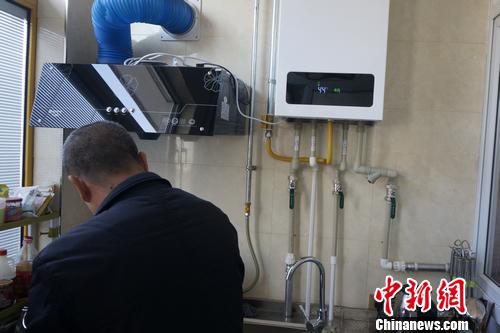 南下温村村民李少富正用燃气灶烧水，一旁的壁挂炉显示供暖温度。汤琪 摄