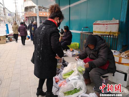寒风凛冽，在甘肃省白银市白银区街头，一位75岁的老人张菊芳蜷坐在街头卖菜，为病逝的儿子还债。　甘芬　摄