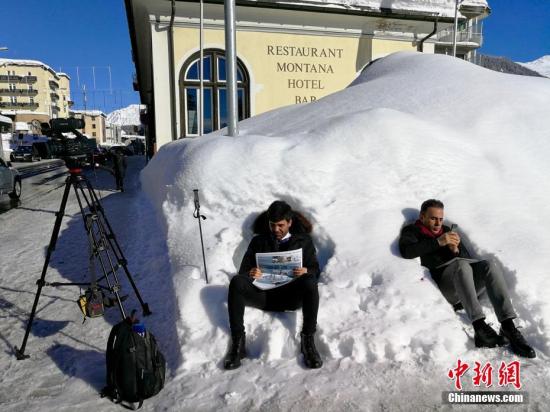 资料图：当地时间2018年1月23日，2018年世界经济论坛年会(“冬季达沃斯”)在瑞士小城达沃斯开幕。今年的冬季达沃斯年会开幕前夕，当地迎来了多年不遇的强降雪。图为两名记者当天坐在积雪上休息。中新社记者 彭大伟 摄