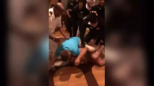 网上视频显示，一名穿蓝色T恤的男子将一名穿着橘色短裤的男子按在酒吧地板上。