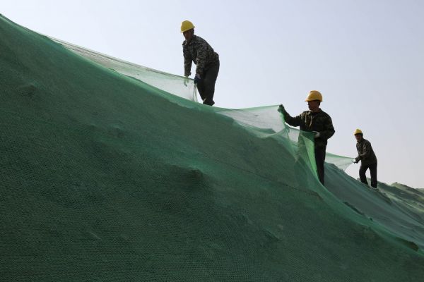 资料图片:2017年11月5日,在山东省滨州市博兴县一处建筑工地,建筑工人在施工现场的土方上覆盖密目网。新华社发