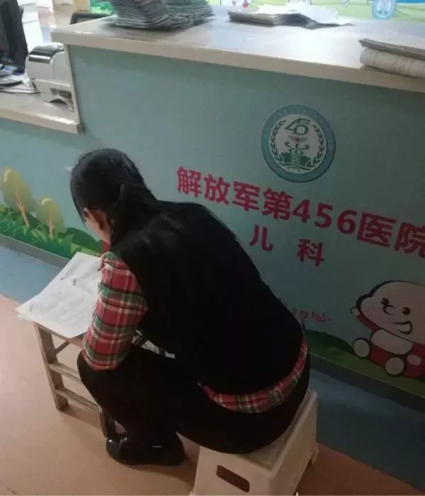 南一女老师陪娃住院,走廊趴板凳上批改试卷到