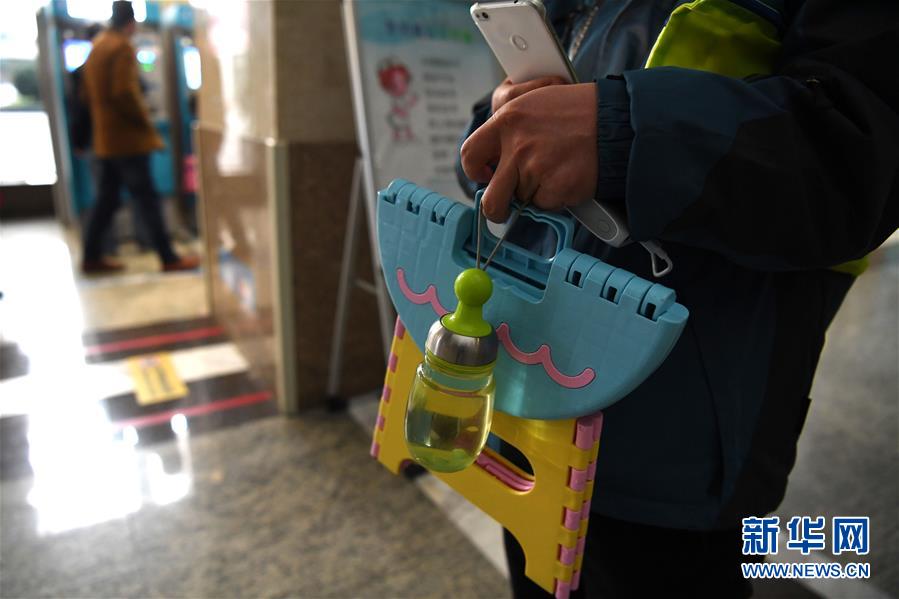 杨召伟在合肥一家医院的自助挂号机前为怀二宝的爱人挂到了妇产科号，板凳、水杯、手机充电宝是他每次排队的必备物品（11月23日摄）。新华社记者 刘军喜 摄
