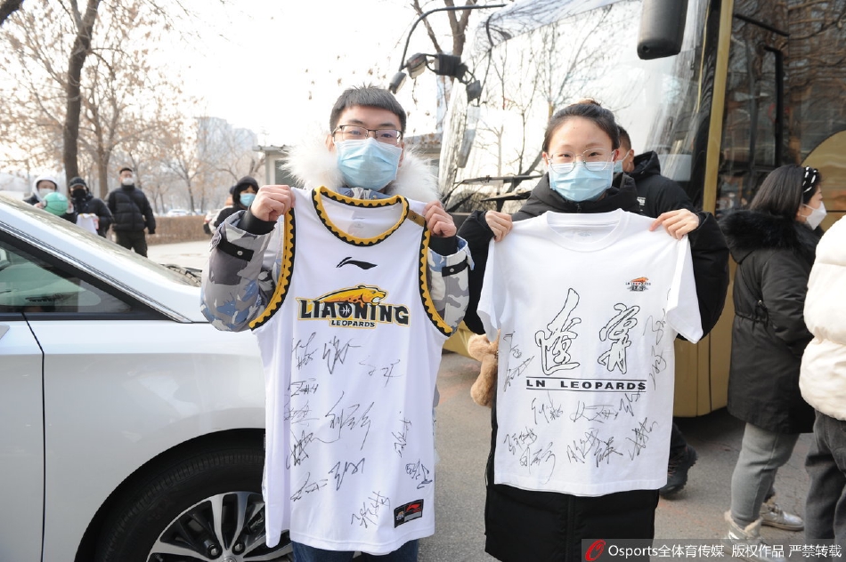 镜头拉近，一位头发花白的老球迷格外引人注目，他戴着厚实的棉帽，双手紧紧握着一幅自制的加油横幅，眼神透过冰冷的空气，执着地望向球员通道的方向，那份坚守令人动容。