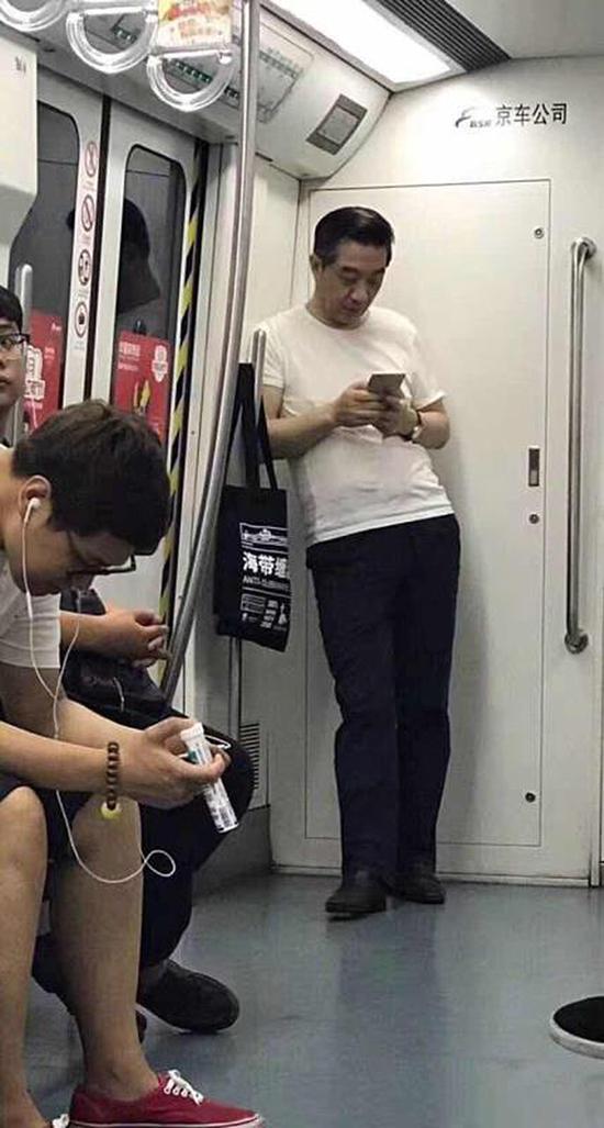 张召忠身着白色T恤，斜倚在地铁车厢内玩手机。&nbsp; 