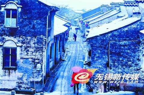 在惠山区玉祁街道,市民从覆盖着一层薄雪的礼社古街街头走过。