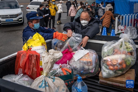 12月26日,在昆明市呈贡区蓝光天娇城小区门口,工作人员正在将食品等物资搬运上车。新华社记者胡超 摄