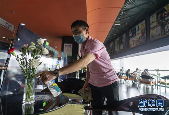 7月20日,昆明市北辰财富中心影院一名保洁人员对观众候场区的桌椅进行消毒。 新华社发(陈欣波 摄)