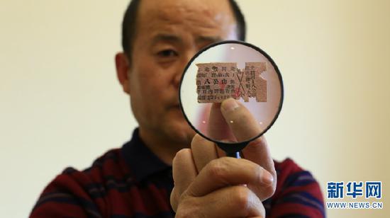 孙昆育用放大镜展示残缺的硬卡纸火车票 新华网 潘越 摄