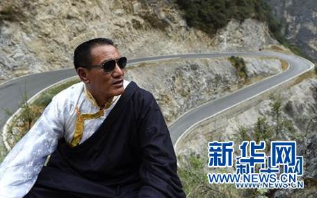 斯那定珠在香格里拉大峡谷内仰望远方(他的一只眼睛近乎失明,经常戴着墨镜),身后是其倾尽所有修建的其中一段公路(2016年5月14日摄)。新华社记者蔺以光 摄