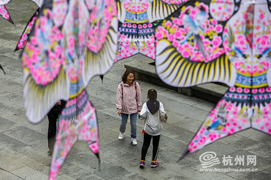 游客们漫步在风筝下享受惬意的时光。