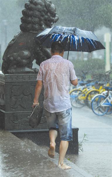 市区新城大道,一名男子光着脚丫提着鞋行走在雨中.