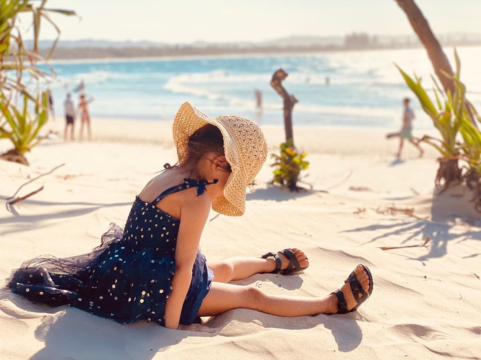 "照片中小周周戴着编织帽坐在沙滩上,穿着蓝色吊带裙,长腿抢镜