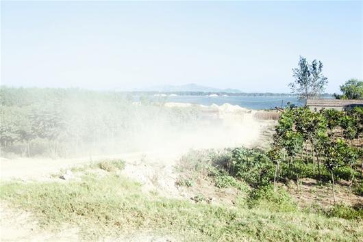 图为:运输车带起的灰尘漫天飞扬,刚刚开过的两辆大卡车淹没在灰尘里