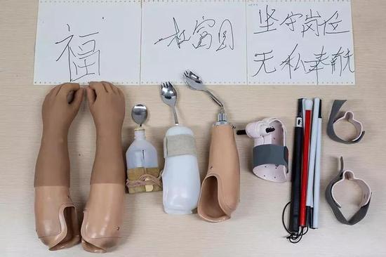 △杜富国使用的义肢、辅助具及其用辅助具写的字。从左至右:美容义肢、第一代吃饭辅助具、第二代吃饭辅助具、第三代吃饭辅助具、写字辅助具和盲杖辅助具。