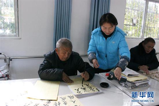 12月2日，河南省驻马店市经济开发区托养中心工作人员为写毛笔字的残疾人提供帮助。新华社发