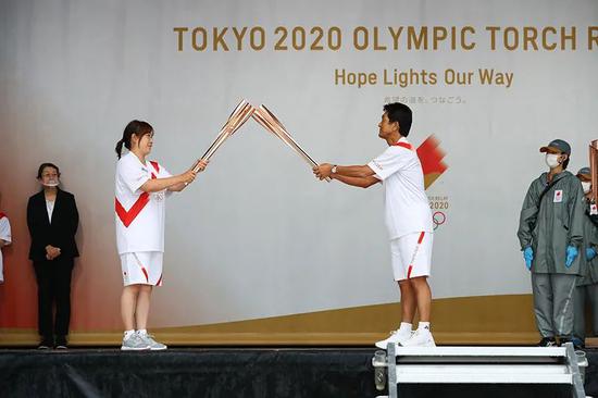 2021年5月12日，日本福冈县北九州市，前日本女排运动员竹下佳江（左前）和前日本网球运动员、东京奥运会日本代表团团长福井烈（右前）在点火仪式舞台上交接火炬。图|新华社