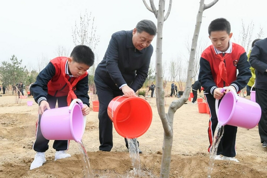 2021年4月2日，习近平总书记来到北京市朝阳区温榆河参加首都义务植树活动。这是习近平总书记同少先队员一起给刚栽下的树苗浇水。新华社记者 李学仁 摄