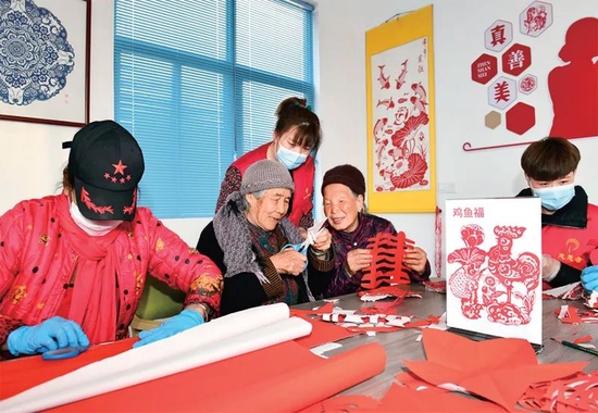  山东省日照市岚山区按照就近、普惠原则建设养老服务中心，并组建志愿服务队为老人提供助餐、助洁、助医等爱心服务。图为2022年2月27日，志愿者在日照市岚山区虎山镇黄家峪村养老服务中心陪老人剪纸、聊天。　新华社记者 郭绪雷/摄
