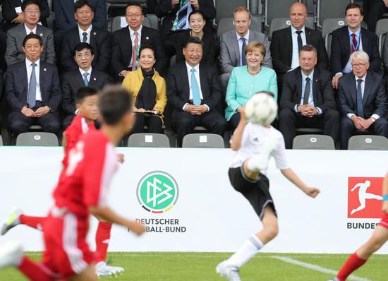 2017年7月5日，国家主席习近平在柏林同德国总理默克尔共同观看中德青少年足球友谊赛。这是习近平主席和夫人彭丽媛同默克尔总理在看台上。