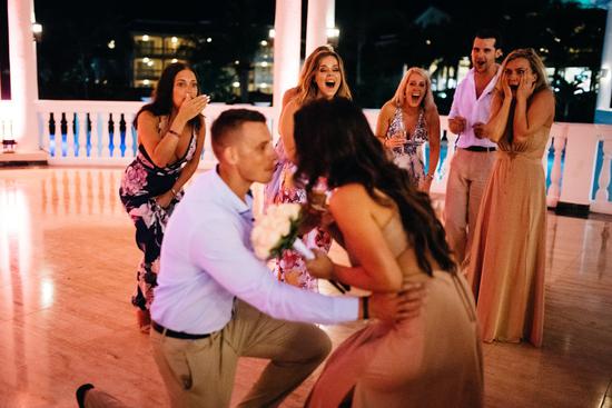 与此同时，亚当在她身后单膝下跪，手中捧着订婚戒指，等待杰西卡转身。