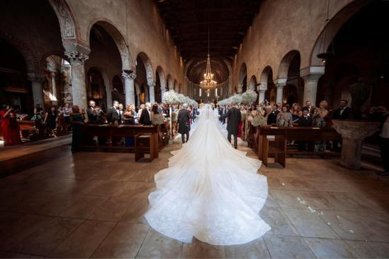 新娘维多利亚在父亲保罗 - 施华洛世奇的陪伴下前往这场奢华的婚礼，身穿的婚纱裙裾与头纱加起来长达 8 米。