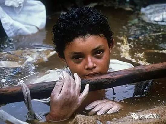 照片中的女孩叫Omayra Sanchez，13岁，哥伦比亚人。在1985年火山爆发所引起的泥石流将她困在泥石中60个小时，一半的身体都浸在泥石中。救难人员一边设法救出，一边安抚她，却可以从她黑如深渊的眼睛中看到绝望，最终女孩还是不幸死亡了……