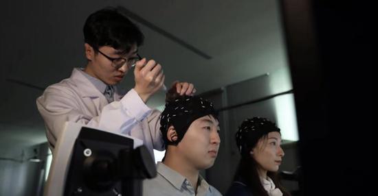学生佩戴脑电帽，专注地盯着屏幕上的方块，完成对机械臂的操控。天津大学供图