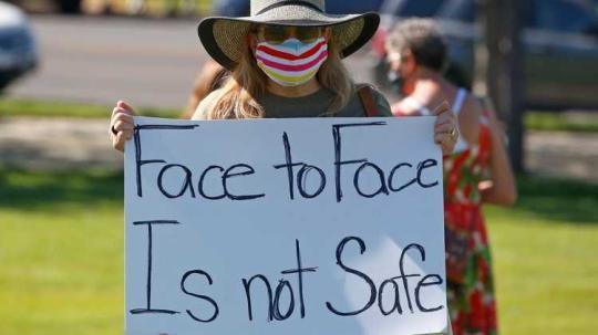 △犹他州一名小学教师举起“面对面不安全”的标语(图片来源：《今日美国报》)