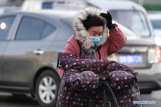 A woman pedals her bicycle against the wind on a street in Chaoyang District, Beijing, capital of China, Dec. 29, 2020. China's meteorological authority on Tuesday renewed an orange alert, the second highest in a four-tier warning system, for a cold wave as a strong cold front has been sweeping across most parts of central and east China from Monday. (Xinhua/Ju Huanzong)