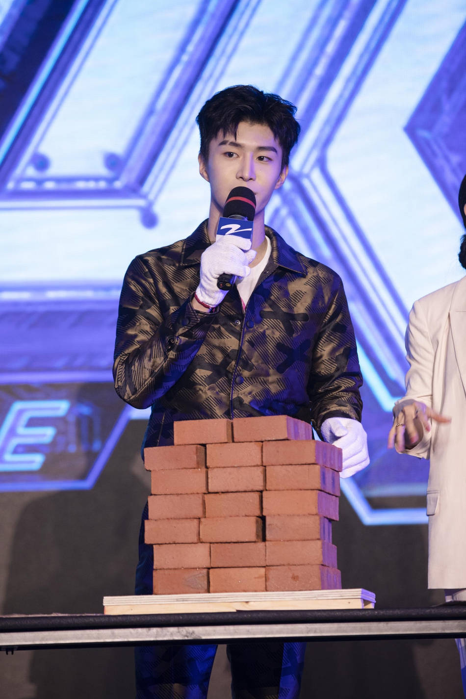 组图:范丞丞着深色花纹套装出席活动 挑战搬砖手握巨型应援棒