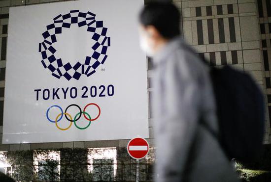 一名戴口罩的行人从挂有东京奥运会标志海报的日本东京都厅大楼前走过。新华社/路透