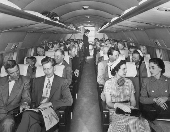 乘客坐在美国传奇飞机客舱内，座位一共四列，乘务员在客舱后部工作。