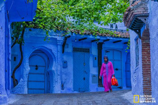 身着桃红色长袍的妇女，行走在蓝色的小巷中，显得格外耀眼。