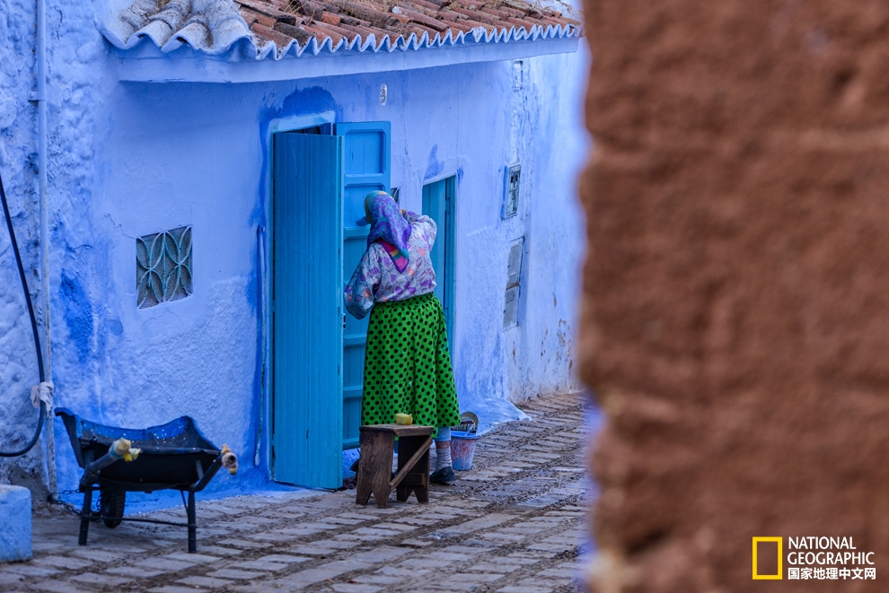 街头转角处一位妇人正在认真给墙壁刷上新鲜的蓝色