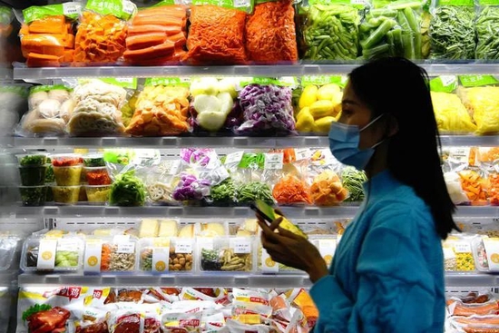 在2021中国预制菜产业大会暨展会现场，一名采购商走过冰冻预制菜食材冷冻柜。图/新华社