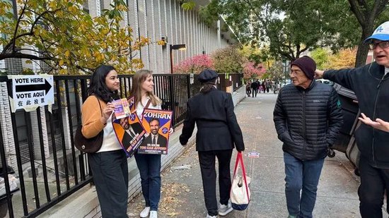  11月4日，支持者在美国纽约一个投票站外手持候选人祖赫兰·马姆达尼的竞选海报（手机拍摄）。新华社发（周焕新摄）