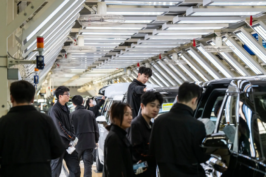 身着黑色工服的工厂工人，站立在电动汽车装配流水线旁。