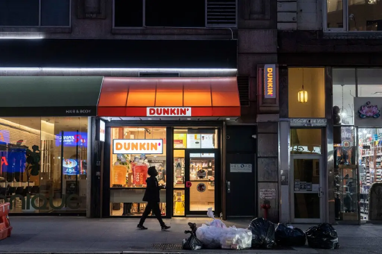一条昏暗的街道上，一家唐恩都乐门店灯火通明，橙色雨篷覆盖着店面入口。