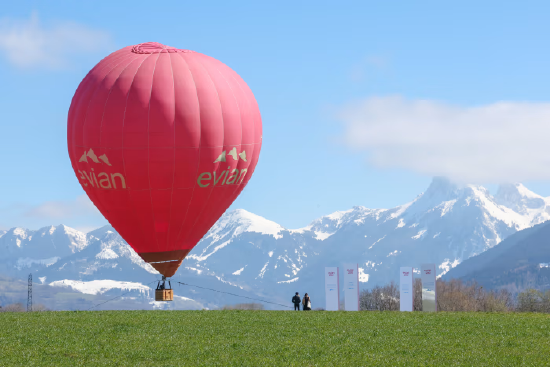 印有依云标志的红色热气球停留在绿地与雪山前，纪念依云矿泉水诞生 200 周年。