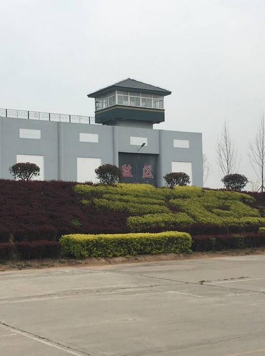 (看守所内,"监区"的灰色高墙和大门)