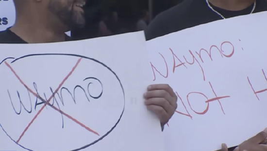 （图：纽约出租车司机在街头抗议 Waymo 自动驾驶测试，高举“Way No to Waymo”口号）