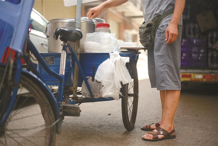 卖豆腐花的手推车上绑着一打白色塑料袋.