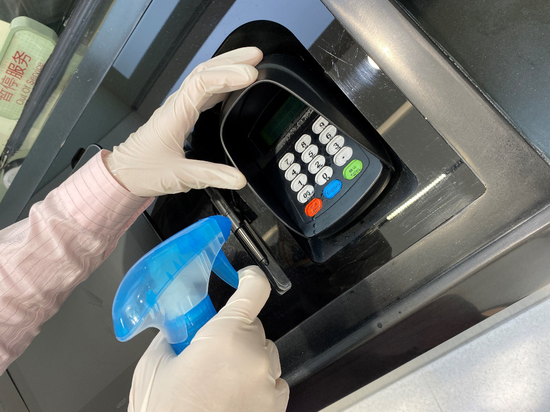 图为运营柜员使用消毒液为密码键盘消毒